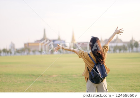 A Traveler Asian woman in 30s, bathed in golden glow of a Bangkok sunset, laughs with carefree joy, her arms outstretched as if to embrace freedom of the moment. Backpack strapped on. A Traveler Asian woman in 30s, bathed in golden glow of a Bangkok sunset, laughs with carefree joy, her arms outstretched as if to embrace freedom of the moment. Backpack strapped on. 124686609