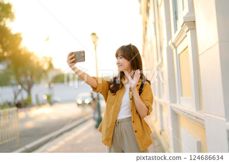Traveler asian woman in her 30s making a livestream and selfie with a smartphone enjoying travel in Bangkok, Thailand. Journey trip lifestyle, world travel explorer or Asia summer tourism concept. Traveler asian woman in her 30s making a livestream and selfie with a smartphone enjoying travel in Bangkok, Thailand. Journey trip lifestyle, world travel explorer or Asia summer tourism concept. 124686634