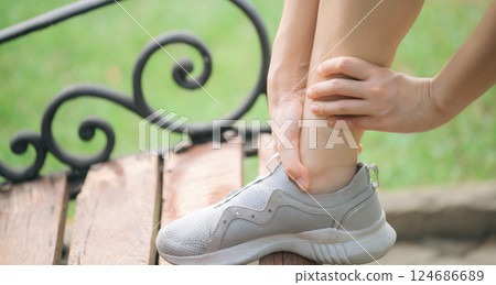 Sprained ankle problem. woman jogger. 30s asian female wearing sportswear holding her ankle with pain after running exercise in public park. 124686689