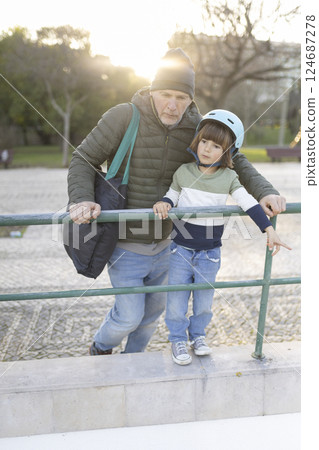 Grandfather and grandson leaning on railing in park at sunset 124687278