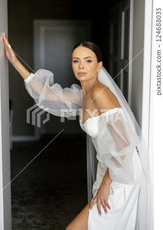 Bride wearing white wedding dress and veil entering room Bride wearing white wedding dress and veil entering room 124688035