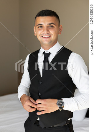 Elegant Groom Getting Ready, Buttoning Waistcoat in Hotel Room Elegant Groom Getting Ready, Buttoning Waistcoat in Hotel Room 124688036