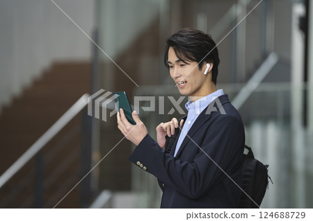 一位年輕商人戴著耳機一邊說話一邊看著智慧型手機螢幕 124688729