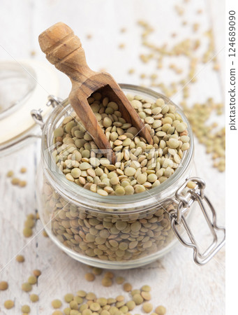 Glass jar full of raw green lentils with a wooden scoop on white table closeup. Dried legumes Glass jar full of raw green lentils with a wooden scoop on white table closeup. Dried legumes 124689090