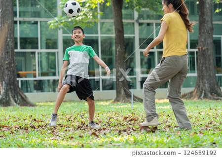 Fun and Bonding Through Soccer. A young boy joyfully plays soccer in the park with his mom. 124689192