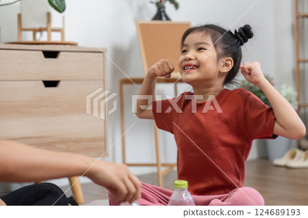 Strength and Joyful Play. A little girl showcasing her muscle with pride during a playful exercise routine. 124689193