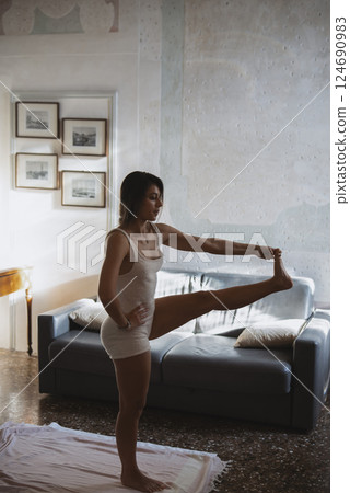 A woman is stretching in her cozy living room, preparing for her yoga practice session 124690983