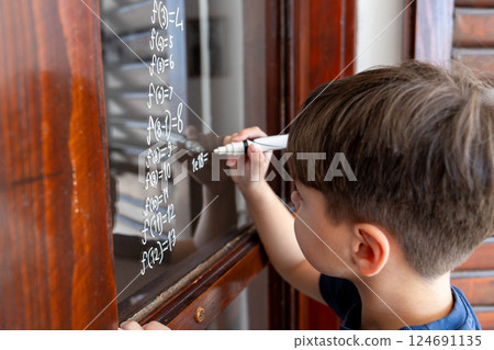 The child writes mathematical formulas on the glass with a marker. The child writes mathematical formulas on the glass with a marker. 124691135