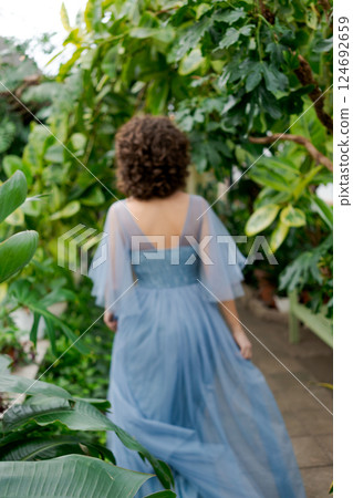 Woman wearing a blue dress is walking through a greenhouse 124692659