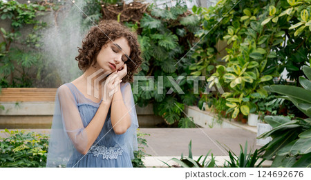 Woman in a blue dress is standing in a garden 124692676
