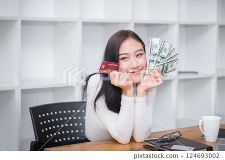 Smiling pretty woman holding credit card and US dollar. Online shopping, e-commerce, internet banking, spending money, working from home concept. 124693002