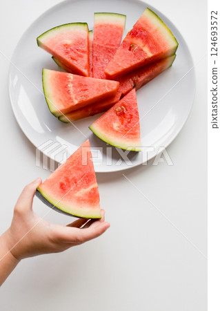 Child hand holding watermelon slice on white plate Child hand holding watermelon slice on white plate 124693572