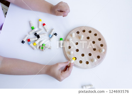 Child playing educational board game with wooden pegs and colored caps 124693576