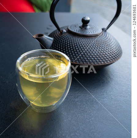 Glass cup with green tea and cast iron teapot on dark table, double wall glass 124693681