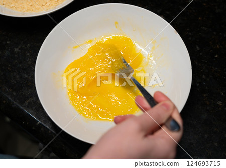 Female hands beat eggs with fork in a bowl, homemade schnitzel cooking process closeup 124693715