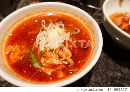a bowl of Korean kimchi red spicy soup with thinly sliced green onions, seafood and spice in a white bowl a bowl of Korean kimchi red spicy soup with thinly sliced green onions, seafood and spice in a white bowl 124693817