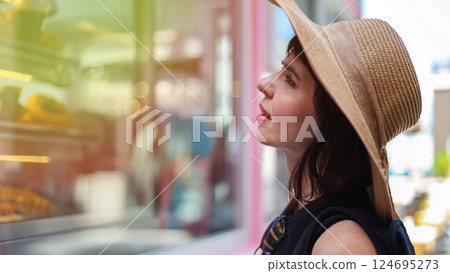 A woman in a summer hat looks at a shop window with interest 124695273