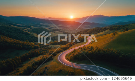 A winding road going into the mountains with a sunset on the horizon. 124695649
