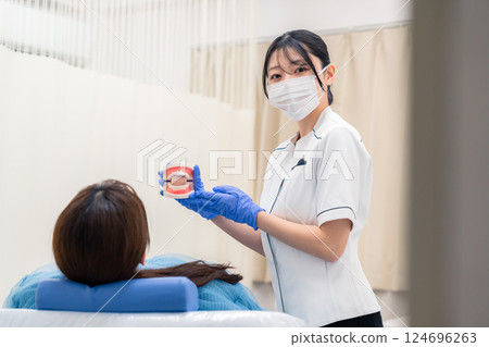 A female dental assistant explaining to a patient using a tooth model A female dental assistant explaining to a patient using a tooth model 124696263