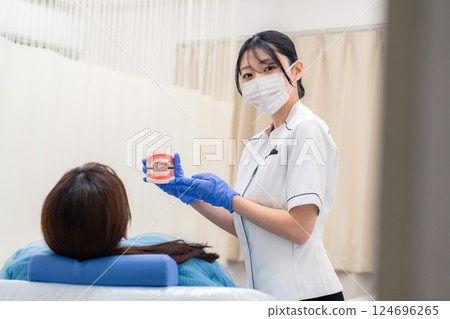 A female dental assistant explaining to a patient using a tooth model 124696265