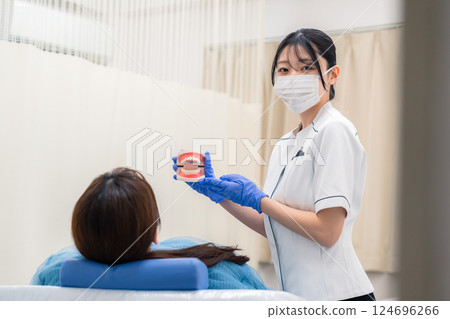 A female dental assistant explaining to a patient using a tooth model A female dental assistant explaining to a patient using a tooth model 124696266