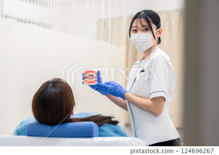 A female dental assistant explaining to a patient using a tooth model 124696267