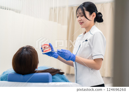 A female dental assistant explaining to a patient using a tooth model A female dental assistant explaining to a patient using a tooth model 124696268