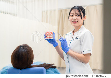 A female dental assistant explaining to a patient using a tooth model A female dental assistant explaining to a patient using a tooth model 124696270