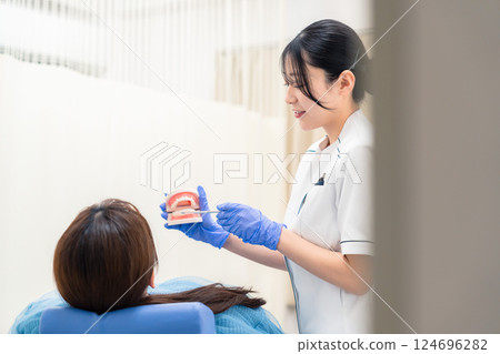 A female dental assistant explaining to a patient using a tooth model A female dental assistant explaining to a patient using a tooth model 124696282