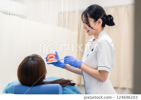 A female dental assistant explaining to a patient using a tooth model 124696283