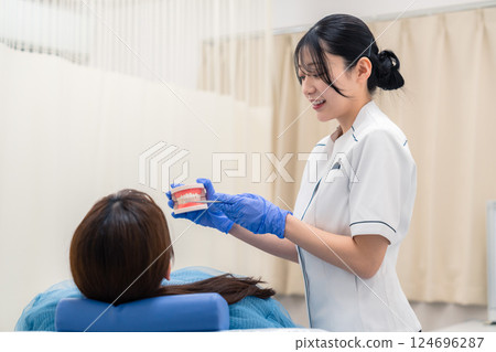 A female dental assistant explaining to a patient using a tooth model A female dental assistant explaining to a patient using a tooth model 124696287