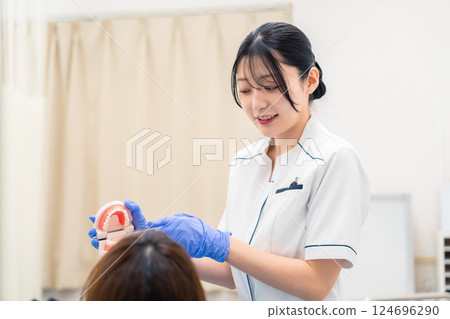 A female dental assistant explaining to a patient using a tooth model 124696290
