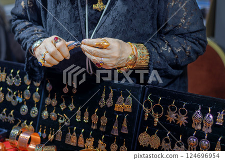 Close-up of female artisan skillfully creating jewelry with tongs, surrounded by handmade gold and silver accessories 124696954