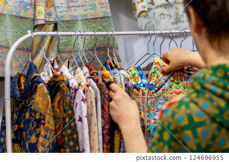 Woman looks at brightly colored folk clothing on rack in store, choosing from variety of colorful traditional patterns 124696955