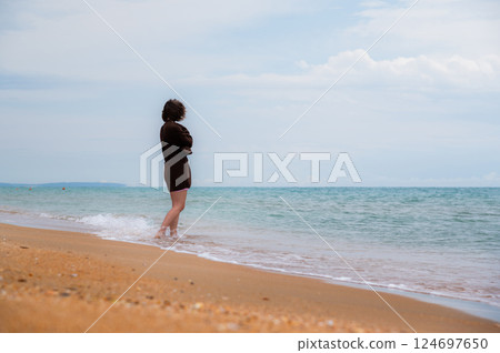 beautiful lonely girl on the beach. young woman secluded on a deserted beach, enjoying rest and tranquility away from the hustle and bustle of cities 124697650