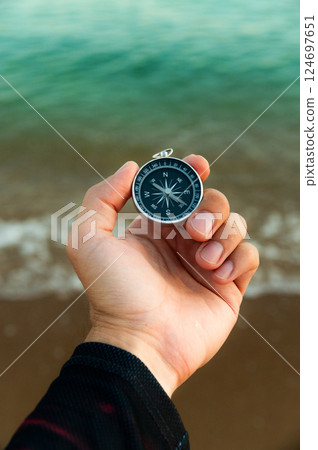 Pov of man hand holding navigational travel compass to find direction and next destination place. Concept of travel people and exploring. Beach and ocean in background Pov of man hand holding navigational travel compass to find direction and next destination place. Concept of travel people and exploring. Beach and ocean in background 124697651