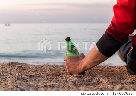 Man's hand holding a bottle of beer on the beach. Close-up of a person relaxing at the sea Man's hand holding a bottle of beer on the beach. Close-up of a person relaxing at the sea 124697652