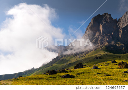 Picturesque view of the mountain with dramatic sky clinging to it, green lush grass at the foot, alpine meadows Picturesque view of the mountain with dramatic sky clinging to it, green lush grass at the foot, alpine meadows 124697657