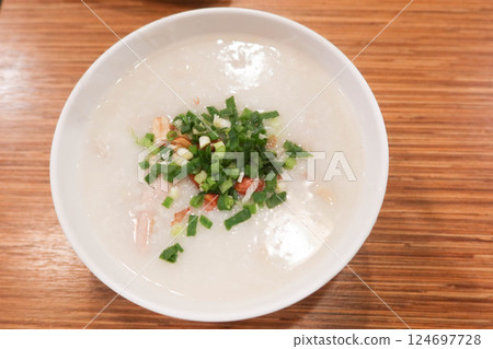 close up of top shot of boiled Chinese congee with spring onion and peanuts on a wooden table with copy space 124697728