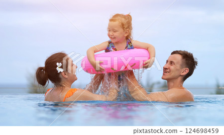Parents lift cheerful toddler girl high above pool water Parents lift cheerful toddler girl high above pool water 124698459
