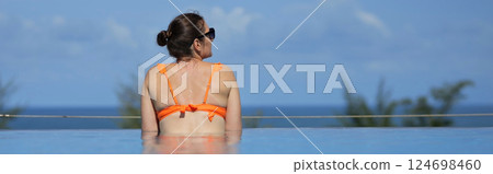 Woman looks out over pool edge leaning on palms against distant greenery 124698460