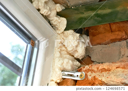 Construction white foam.Installation of a metal plastic window in a brick wall 124698571