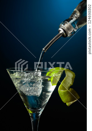 Vodka or gin is poured into a glass with ice. Vodka or gin is poured into a glass with ice. 124698802