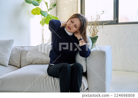 Middle aged unhappy woman experiencing neck joint pain sitting on sofa at home Middle aged unhappy woman experiencing neck joint pain sitting on sofa at home 124698808