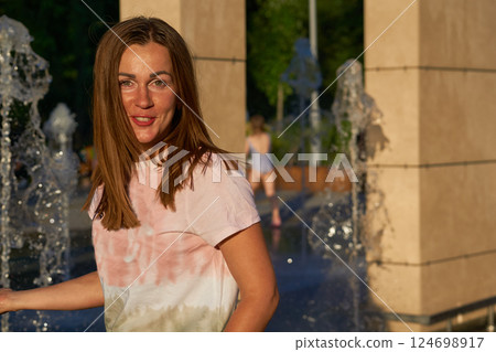 Young happy woman in wet t shirt near fountains in city park Young happy woman in wet t shirt near fountains in city park 124698917