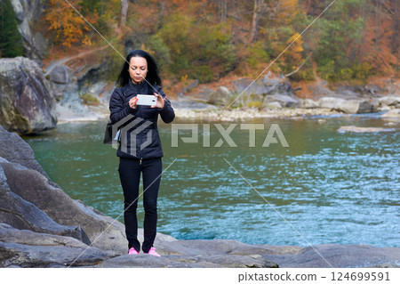A young woman takes a photo near a rocky mountain river with a rapid flow 124699591