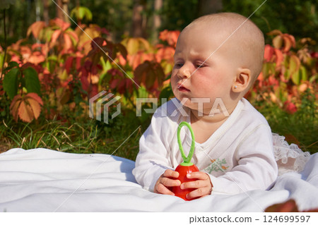 Dissatisfied little baby crawling on blanket on warm summer day in park 124699597