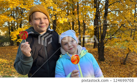 Portrait of a boy and a girl eating lollipops in an autumn park. 124699708