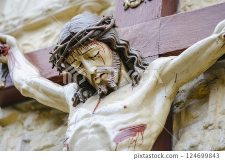 Close-up of a detailed crucifixion statue, showing intricate craftsmanship in the depiction of the figure's face, crown of thorns, and body on the cross Close-up of a detailed crucifixion statue, showing intricate craftsmanship in the depiction of the figure's face, crown of thorns, and body on the cross 124699843