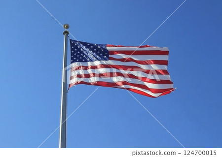 American flag flying proudly against a clear blue sky, with its red and white stripes and stars visible as it ripples in the breeze 124700015